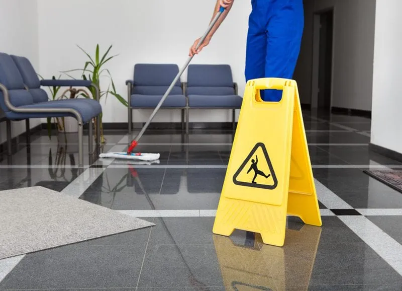 A cleaner mopping a tiled office reception floor beside a wet floor sign