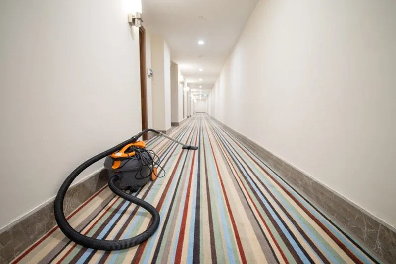 A vacuum cleaner on a long carpeted corridor in a shared building